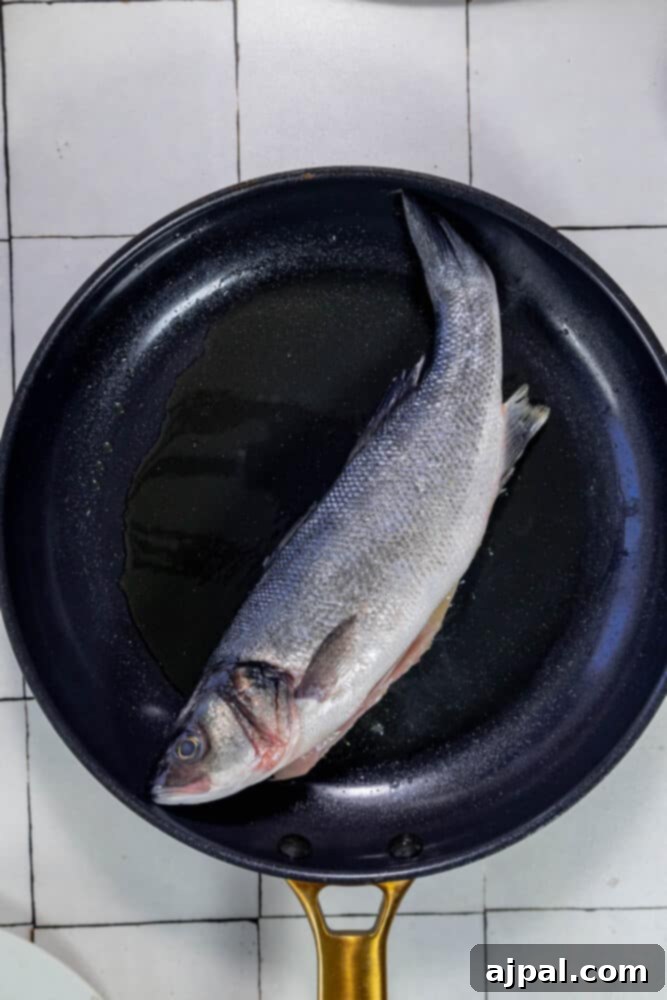 Roasted Branzino with Zesty Lemon-Caper Butter 6 A branzino fish being carefully cooked in a frying pan, surrounded by lemon slices and melting butter.