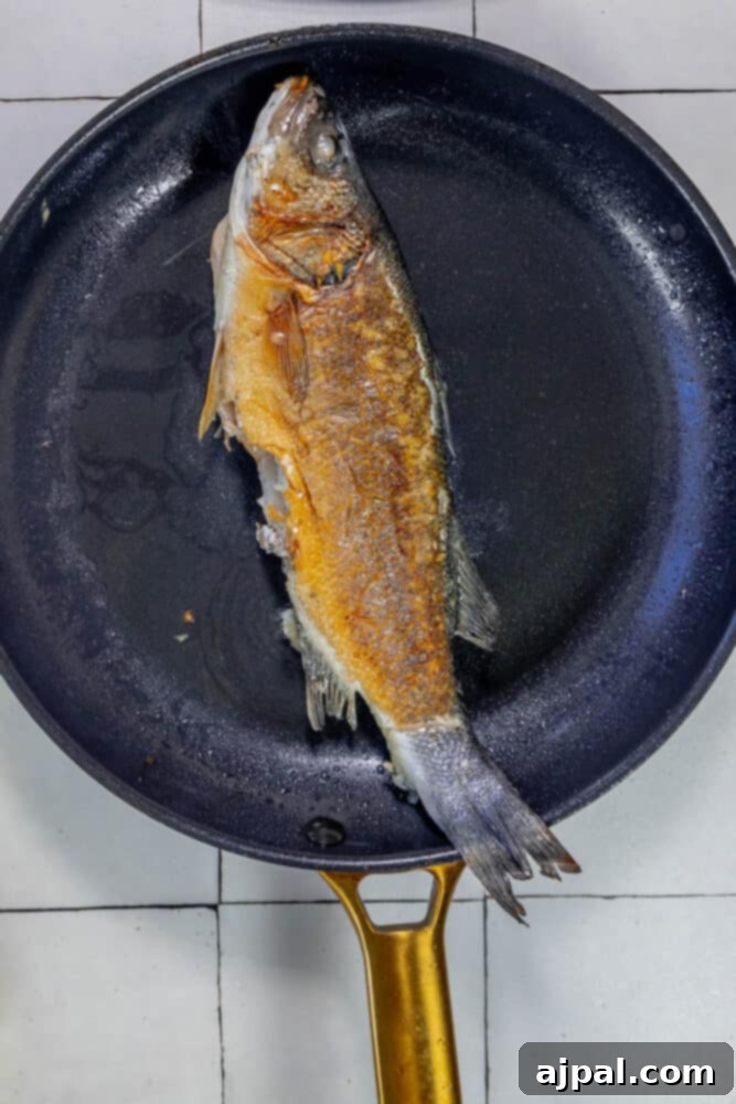 Roasted Branzino with Zesty Lemon-Caper Butter 7 A branzino fish cooking in a pan, infused with lemon and butter, illustrating the early stages of preparation.