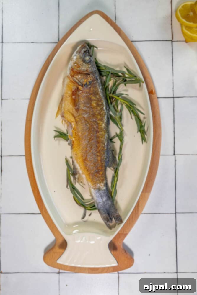 Roasted Branzino with Zesty Lemon-Caper Butter 8 A prepared fish on a plate, delicately garnished with fresh lemon and sprigs of rosemary, awaiting roasting.