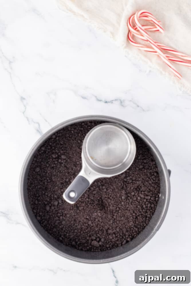 Peppermint Bark Cheesecake 7 A bowl of cocoa powder with a spoon, next to whole and crushed candy canes, on a light colored surface.