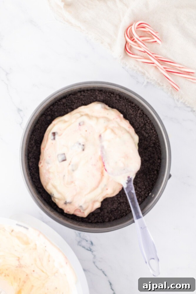 Peppermint Bark Cheesecake 9 A bowl filled with cheesecake batter mixed with crushed candy canes, next to a spoon on a marble surface.