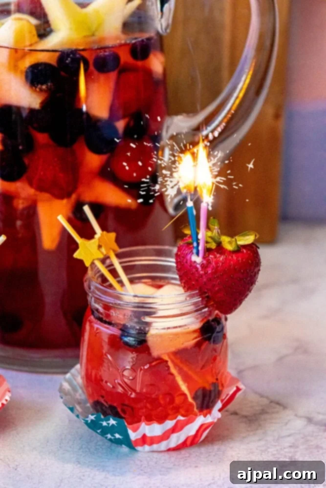 Stars and Stripes Celebration Punch 2 fruit punch with red white and blue fruit in it and a sparkling candle sticking out of a strawberry on the rim of the glass