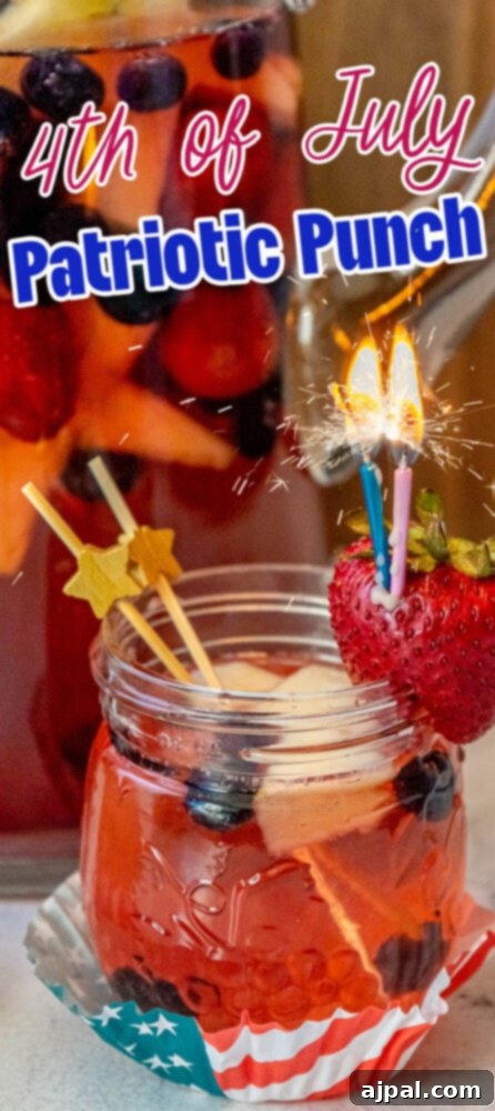 Stars and Stripes Celebration Punch 12 fruit punch with red white and blue fruit in it and a sparkling candle sticking out of a strawberry on the rim of the glass