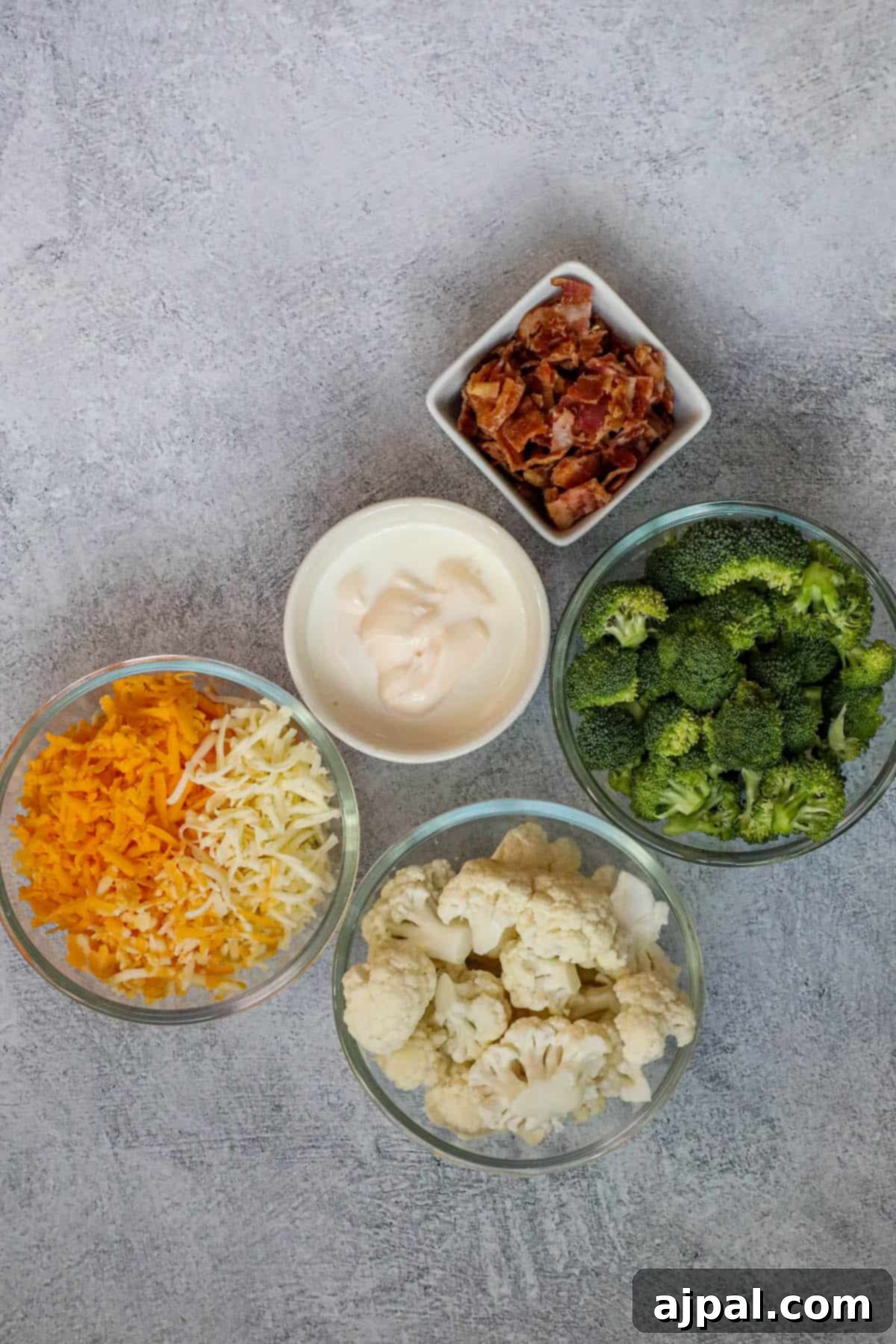 Four bowls containing perfectly portioned servings of creamy broccoli, cauliflower, and bacon casserole.