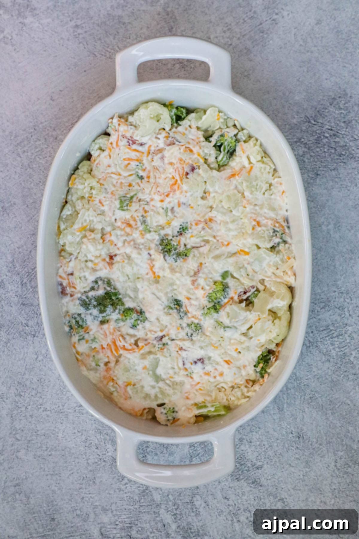 A white rectangular baking dish filled with the unbaked mixture of broccoli, cauliflower, cheese, and bacon.