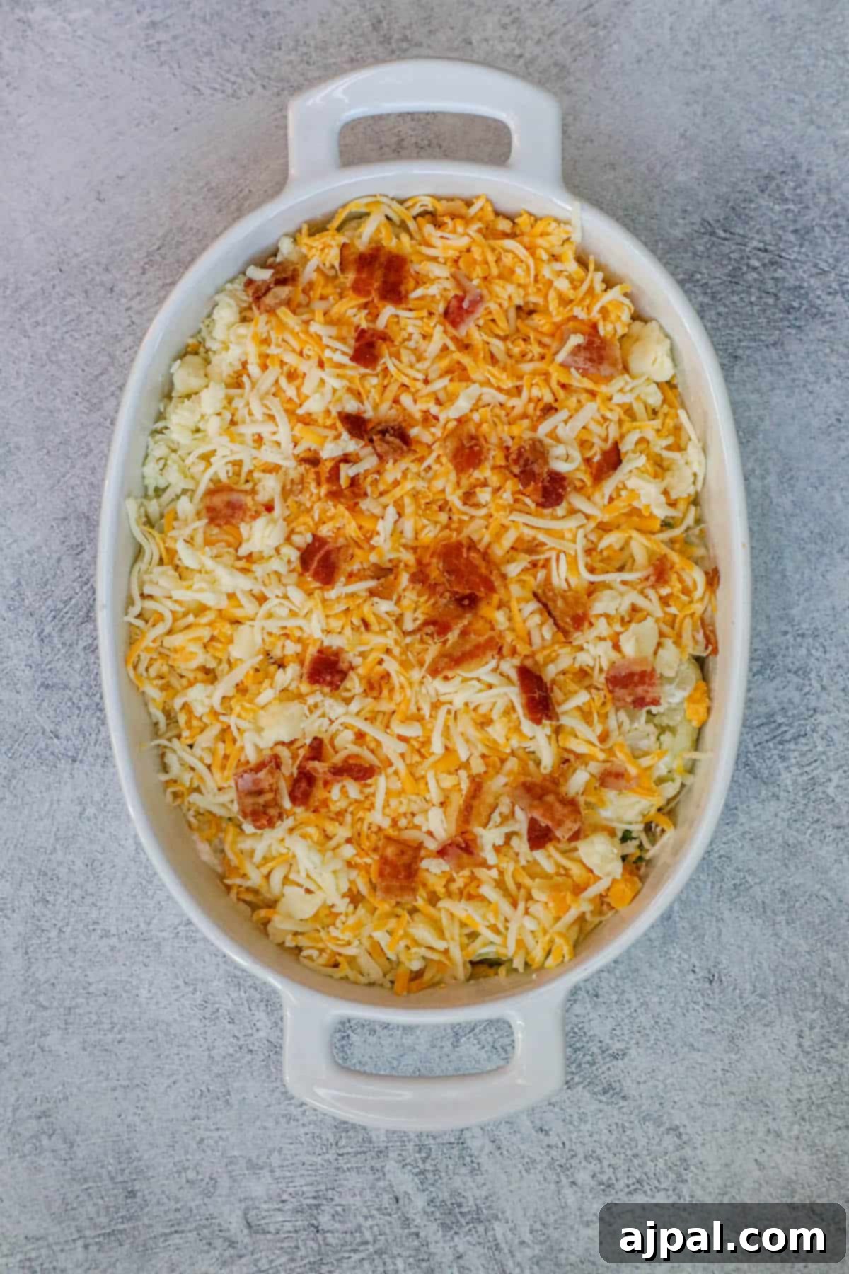 A freshly baked broccoli and cauliflower casserole dish, generously topped with melted cheese and crispy bacon bits.