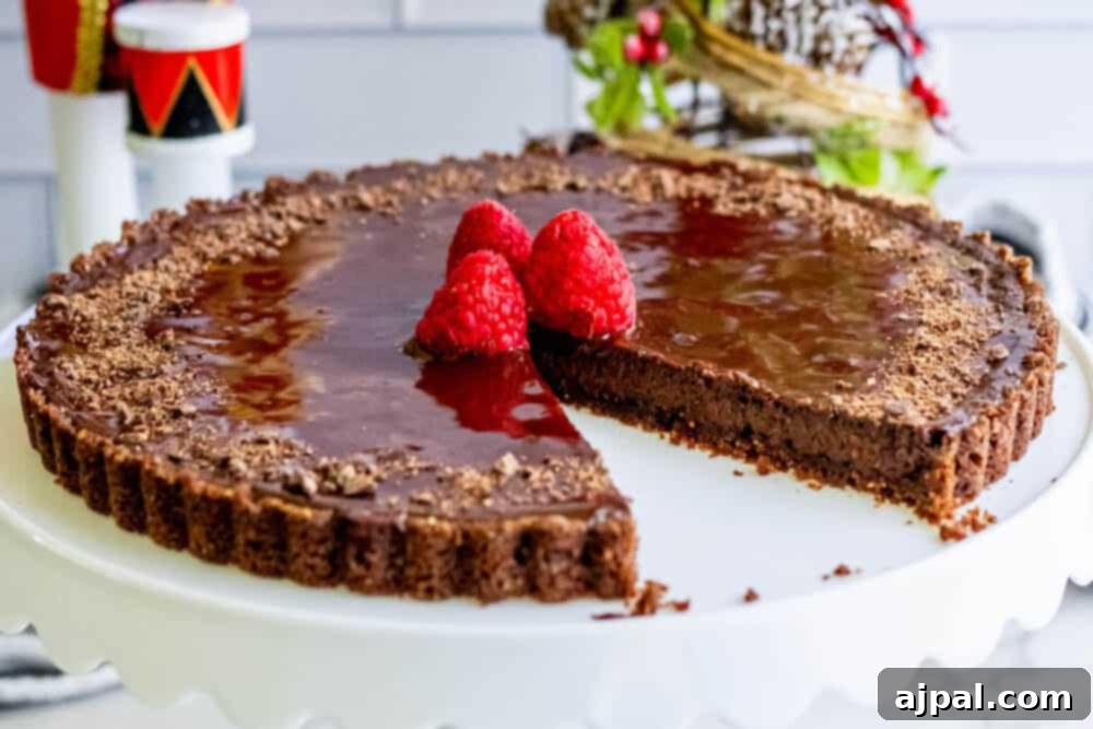 A silky chocolate tart decorated with fresh raspberries on a white serving plate.