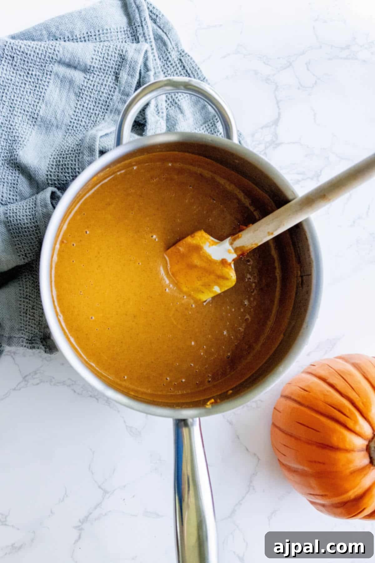 A pot of rich, orange pumpkin pie puree with a spoon resting in it, ready for the next step of preparation.