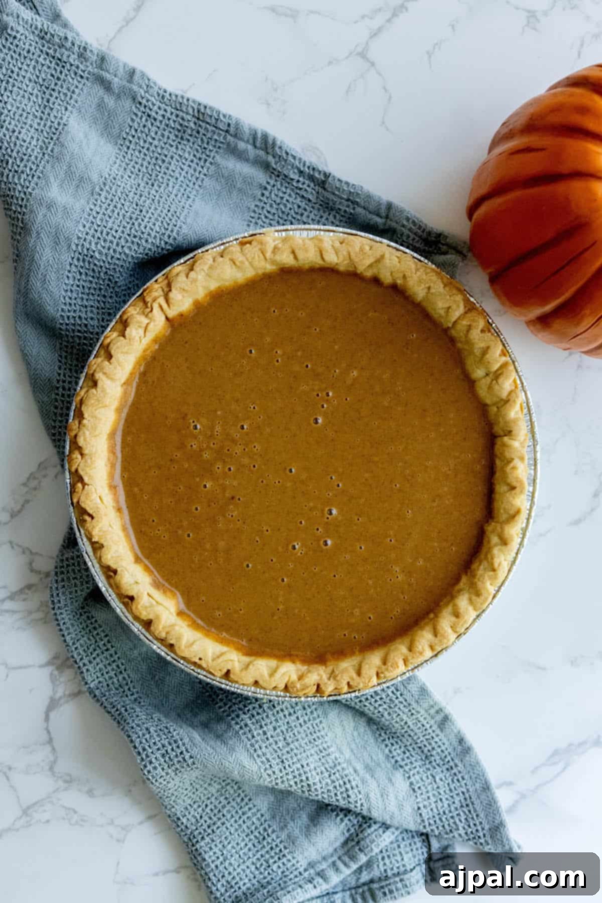 A freshly baked pumpkin pie sits on a rustic wooden table, ready for cooling and serving.