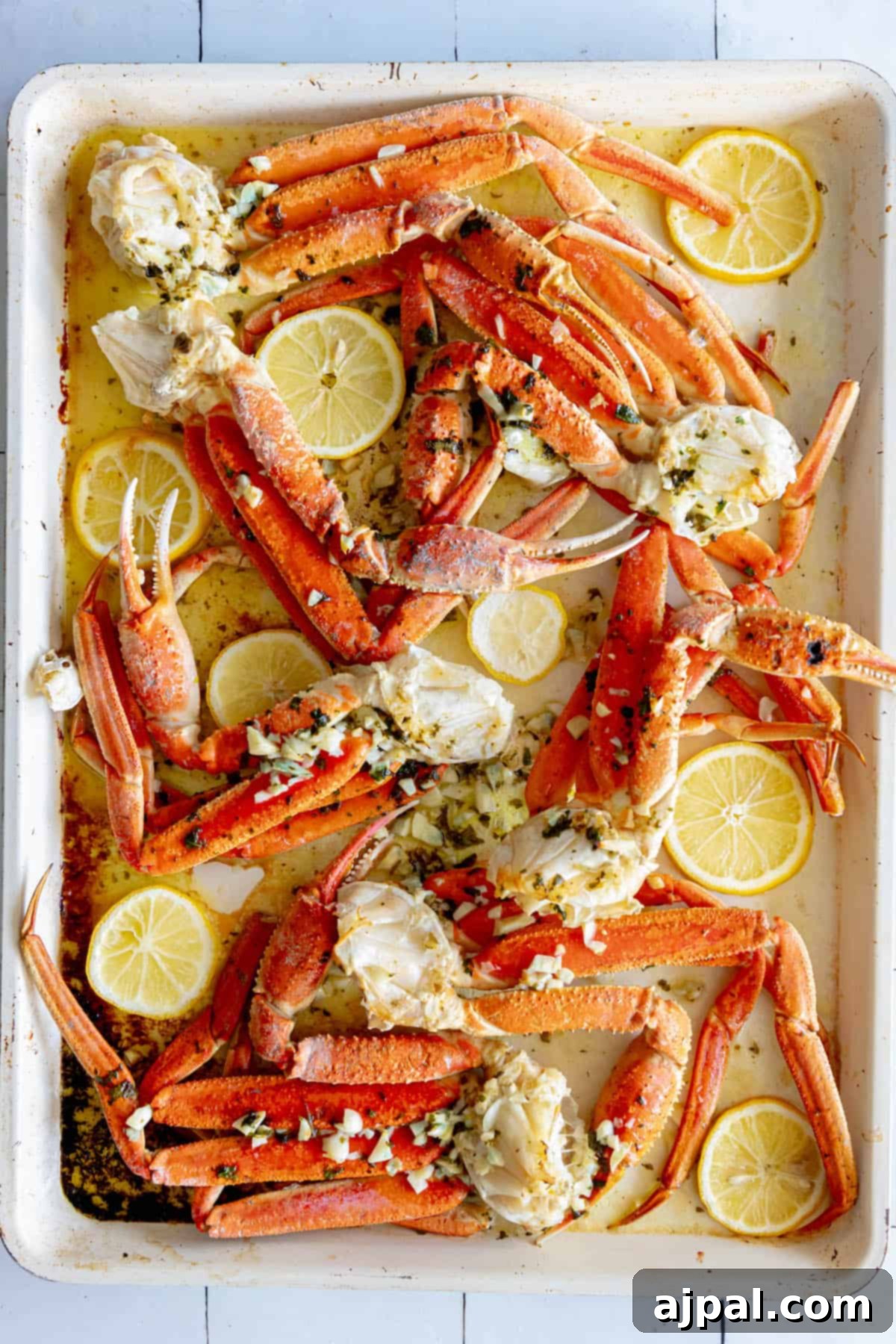 A baking sheet with baked snow crab legs and lemon wedges on it.