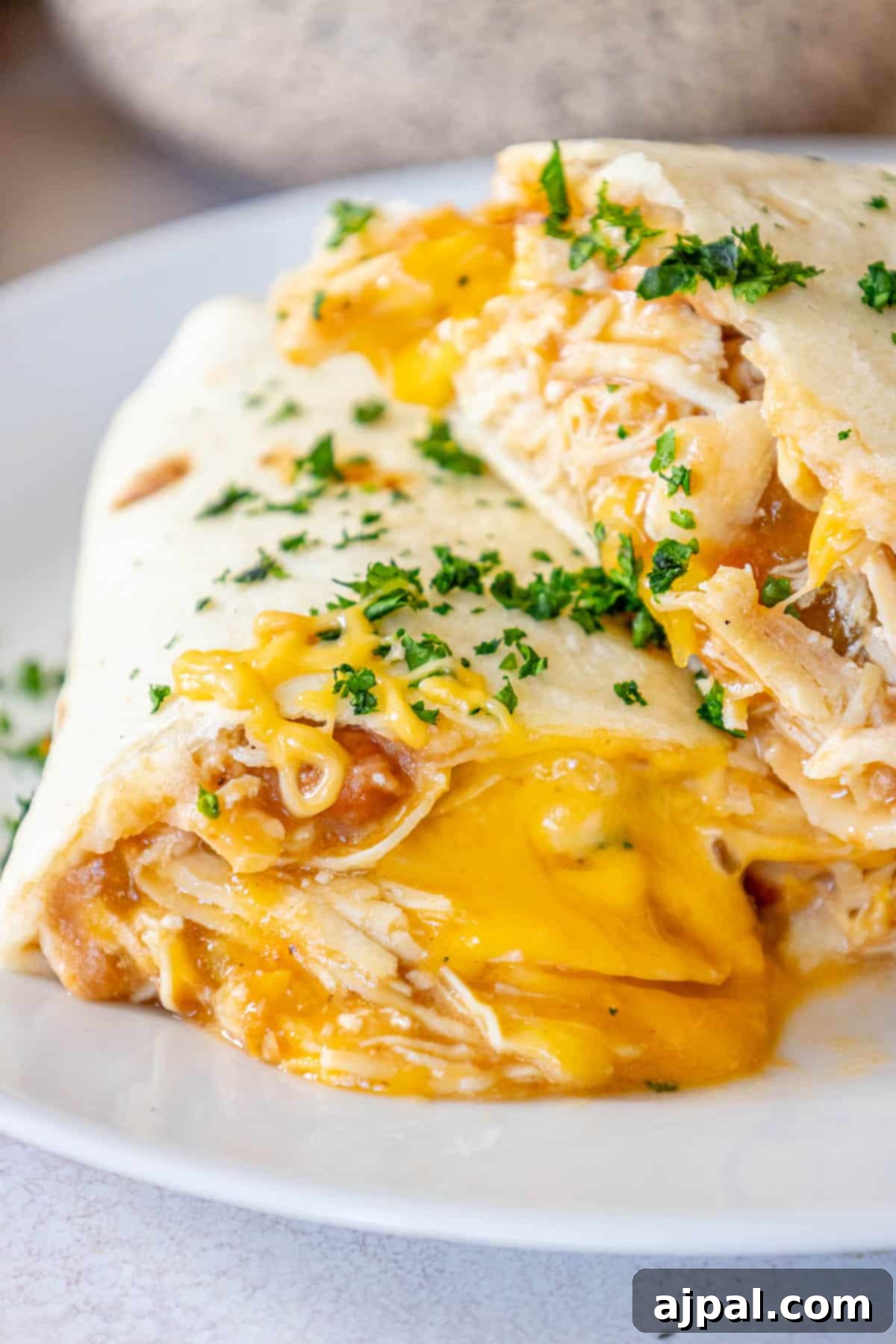 Oven-Baked Chicken Chimichangas 2 Baked cheesy chicken chimichanga on a white plate, garnished.