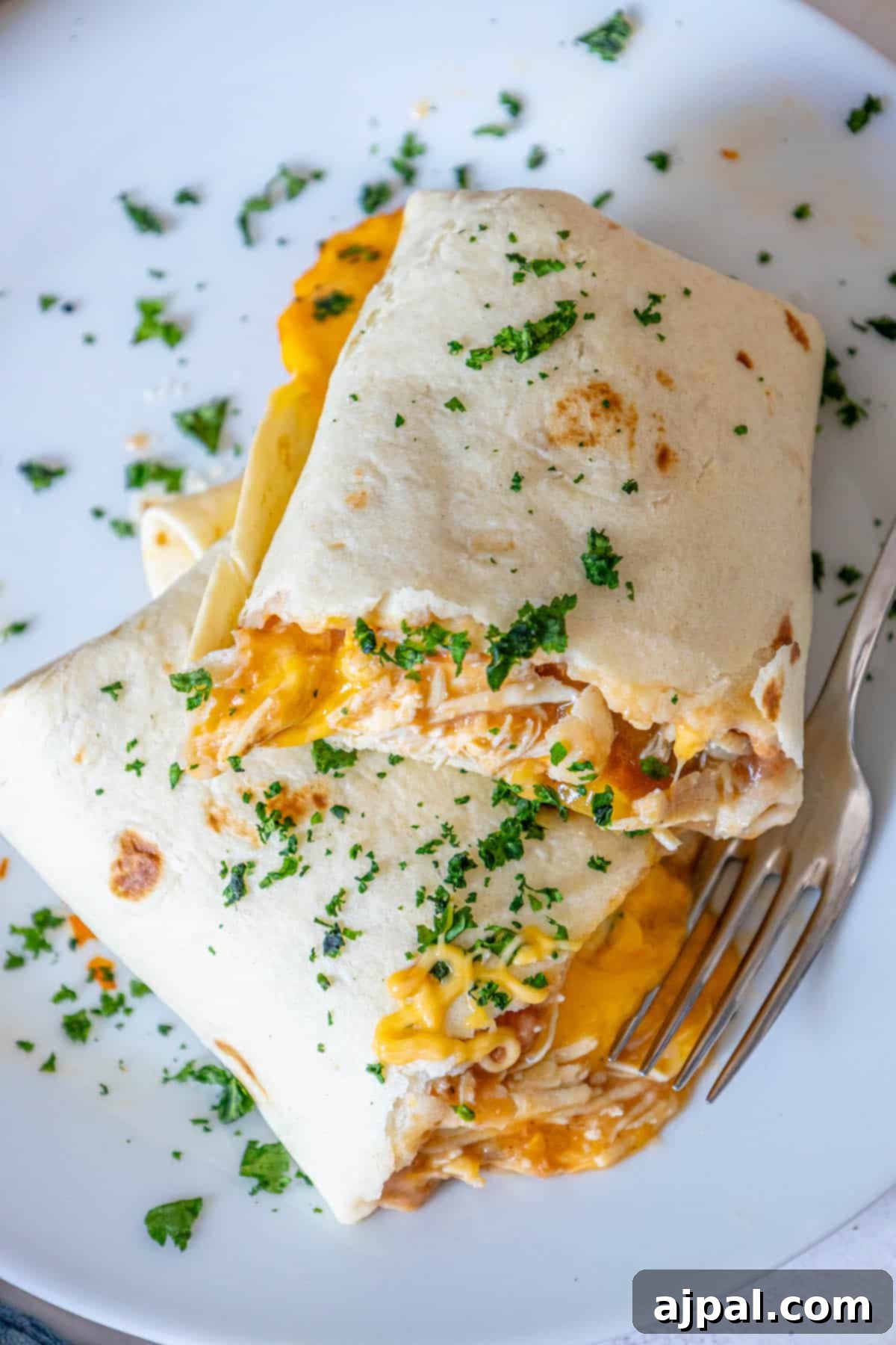 Oven-Baked Chicken Chimichangas 15 Baked chicken chimichanga on a white plate with a fork, ready to eat.