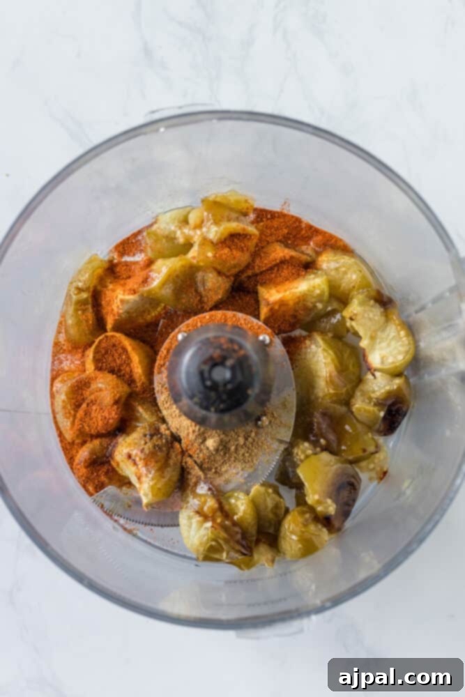 Smoky Chipotle Blaze 8 A food processor bowl filled with colorful ingredients, including roasted tomatillos, garlic, and spices, ready to be blended into Chipotle Hot Salsa.