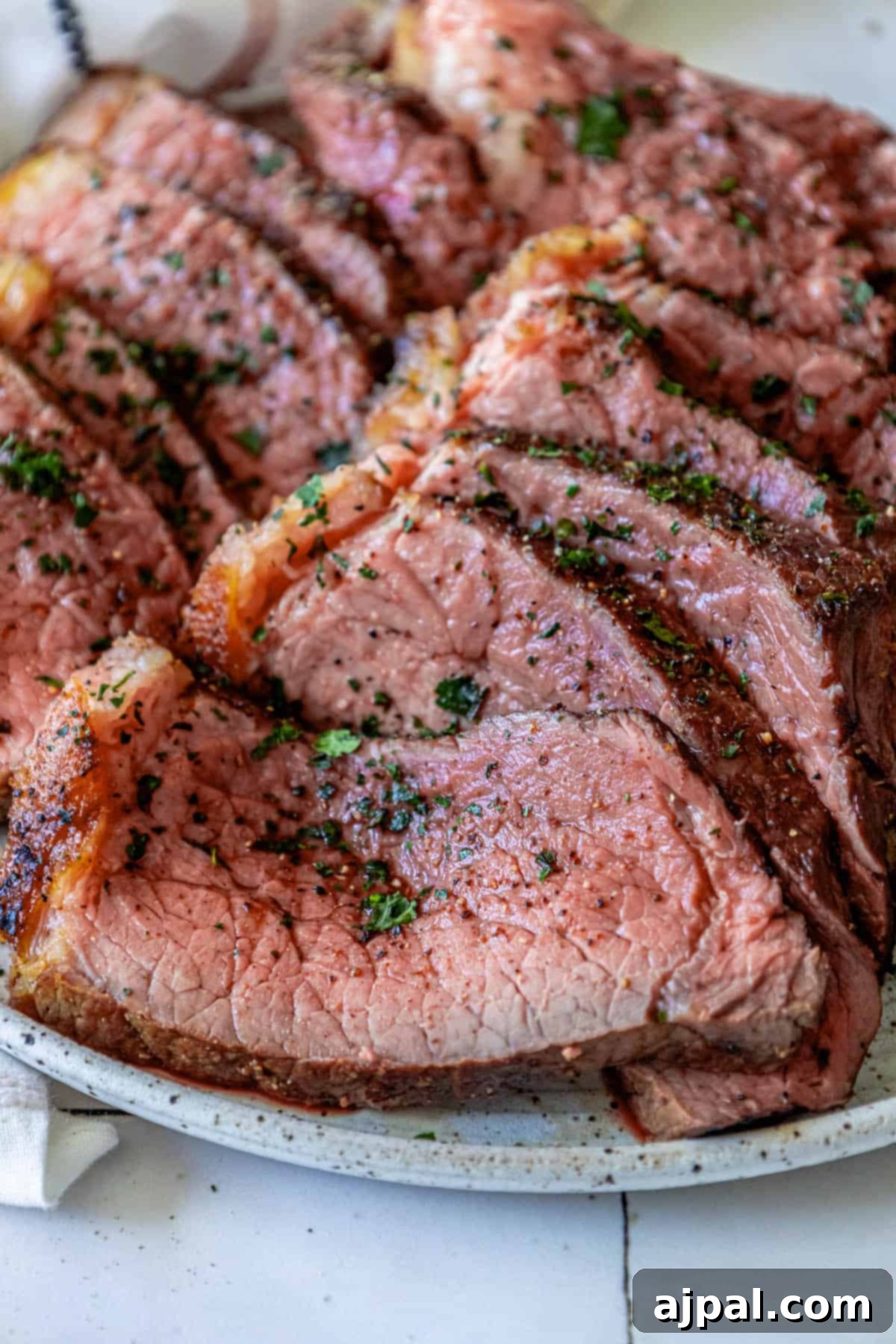 A plate of sliced bottom round roast beef on a white plate, garnished with fresh herbs.