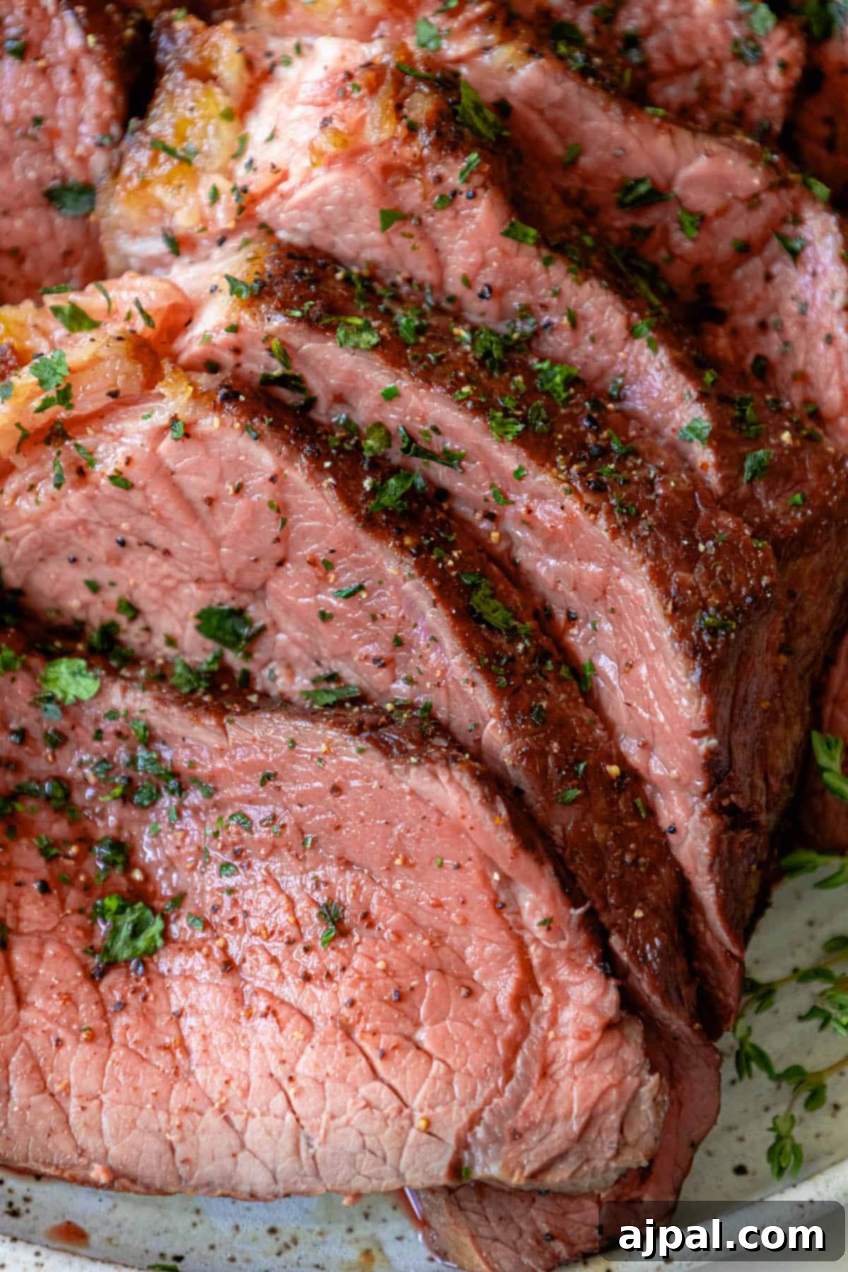 A succulent plate of Bottom Round Roast with Herb Butter on a white plate, showcasing its golden-brown crust and juicy interior.