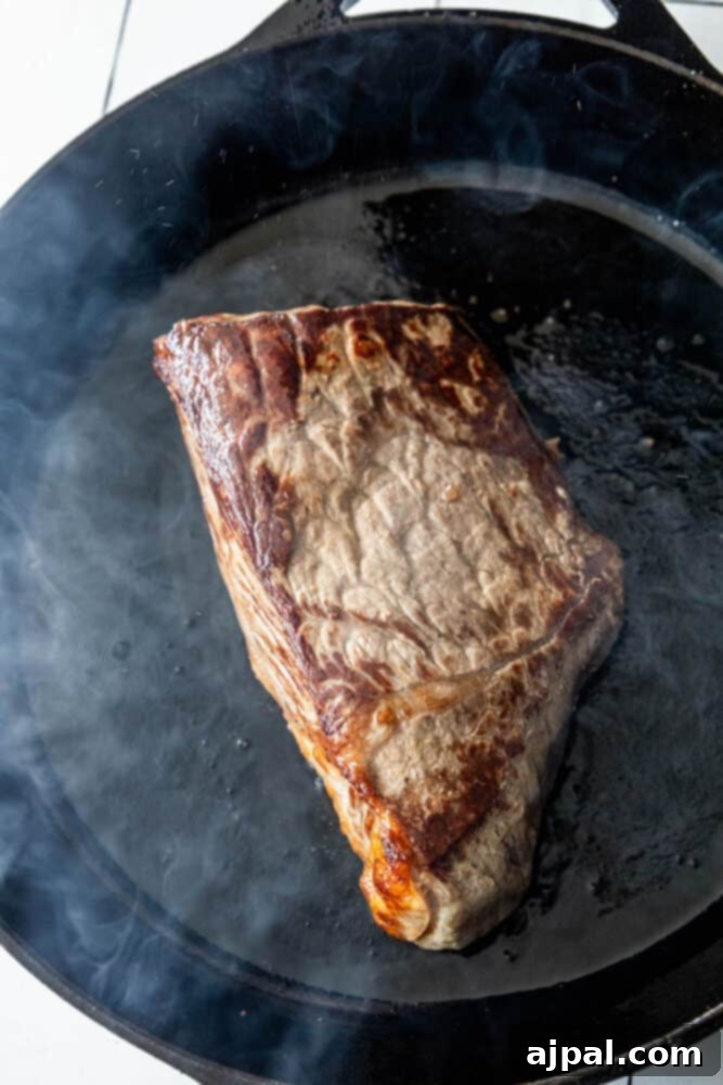 A Bottom Round Roast with Herb Butter is being cooked in a frying pan.