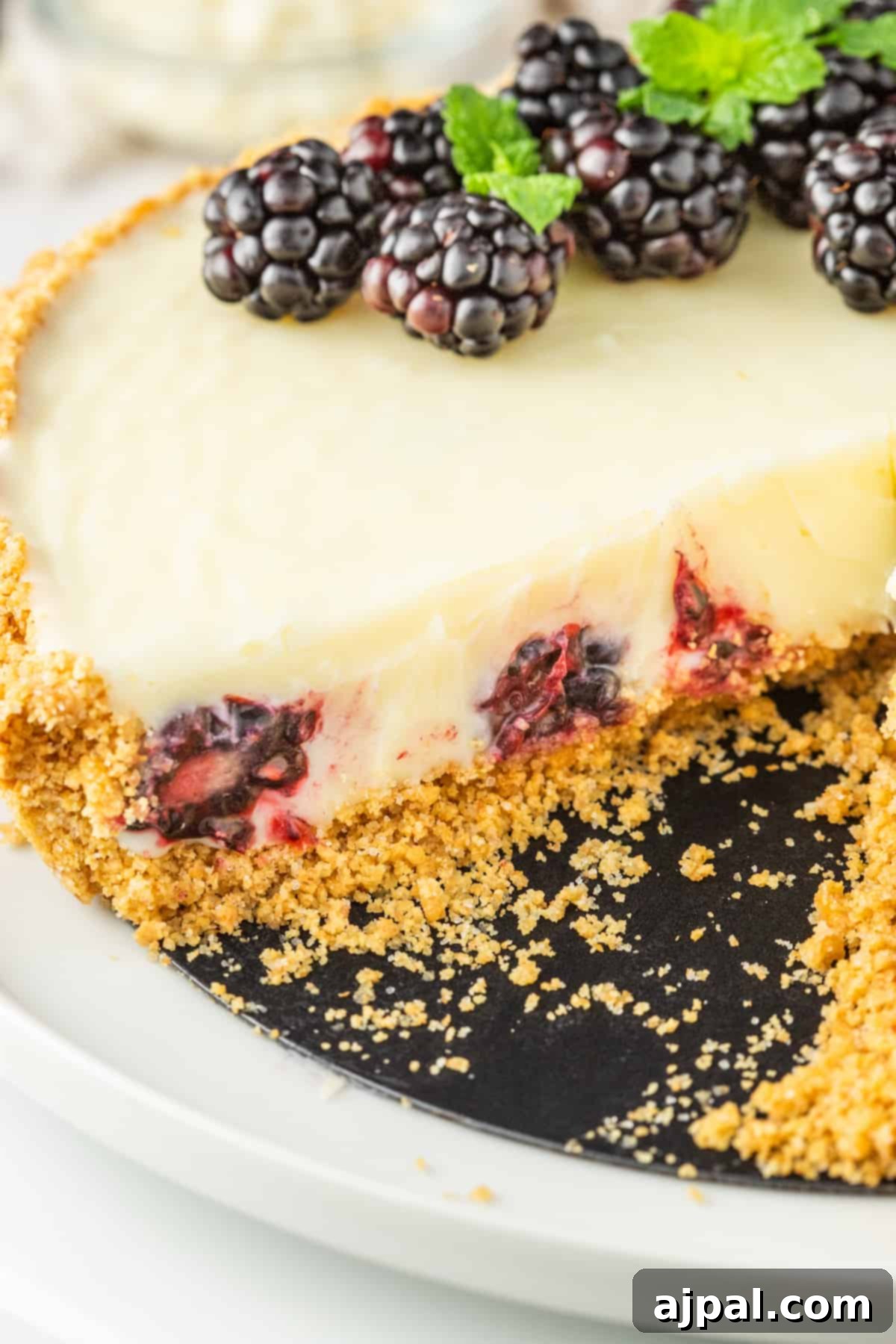 Silken White Chocolate Blackberry Tart 15 A white chocolate blackberry tart on a plate with a slice taken out, showcasing the perfect texture and fruit filling.