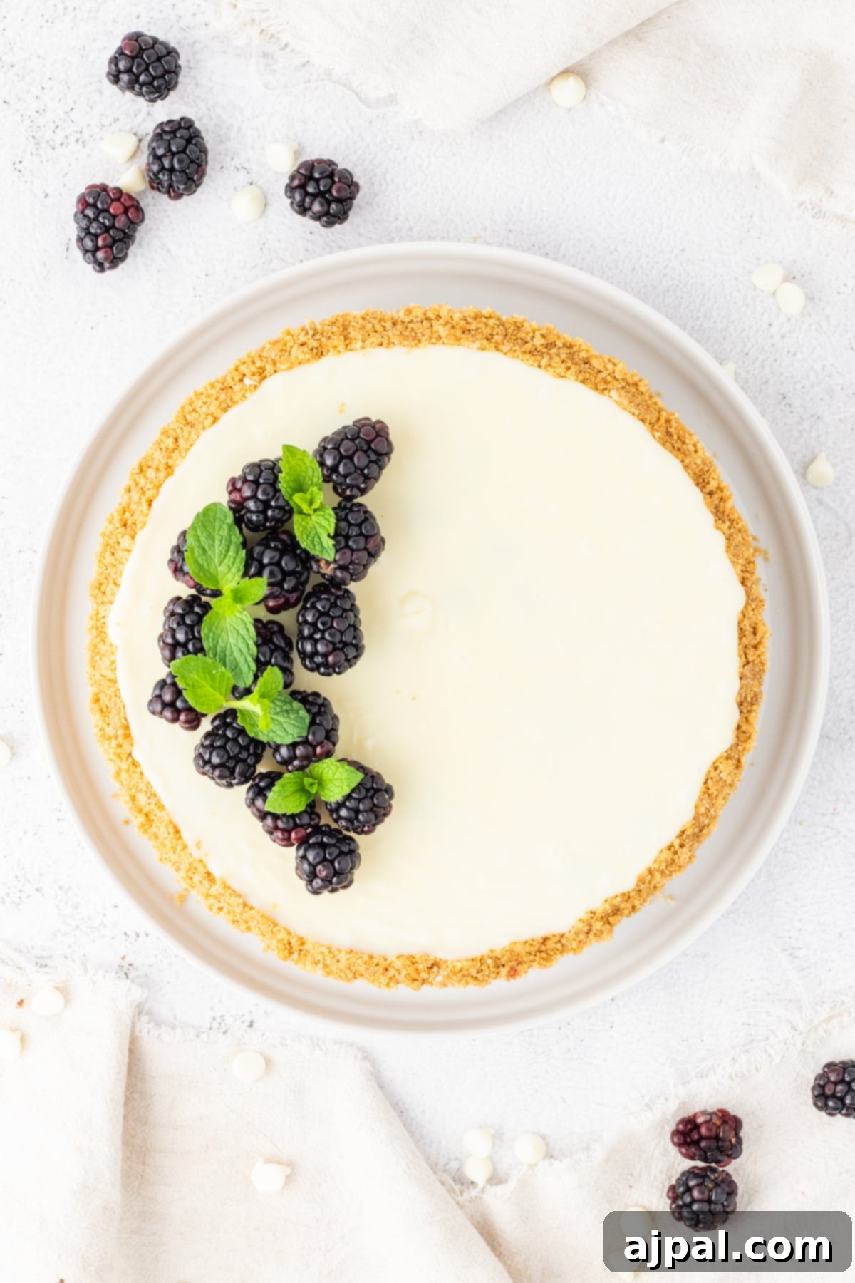 Silken White Chocolate Blackberry Tart 4 A heavenly white cheesecake adorned with plump blackberries and fresh mint leaves, elegantly presented on a pristine white plate, ready to be enjoyed.