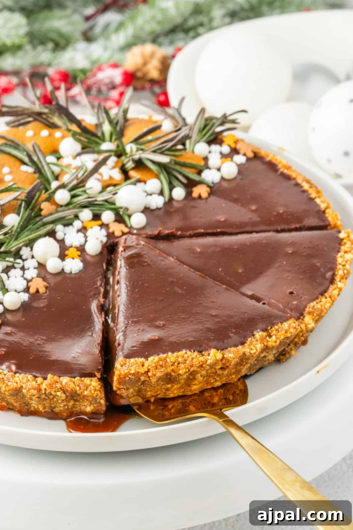 A festive gingerbread chocolate tart garnished with fresh rosemary, presented on a white plate, perfect for the holidays.