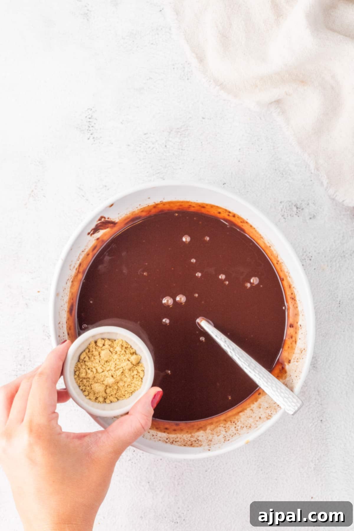 A person holding a bowl of rich chocolate sauce, a key component in the Gingerbread Chocolate Caramel Tart Recipe.