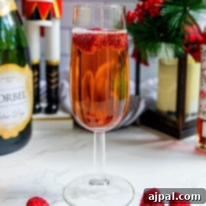 A glass of raspberry champagne sparkler with raspberries and a bottle of champagne.