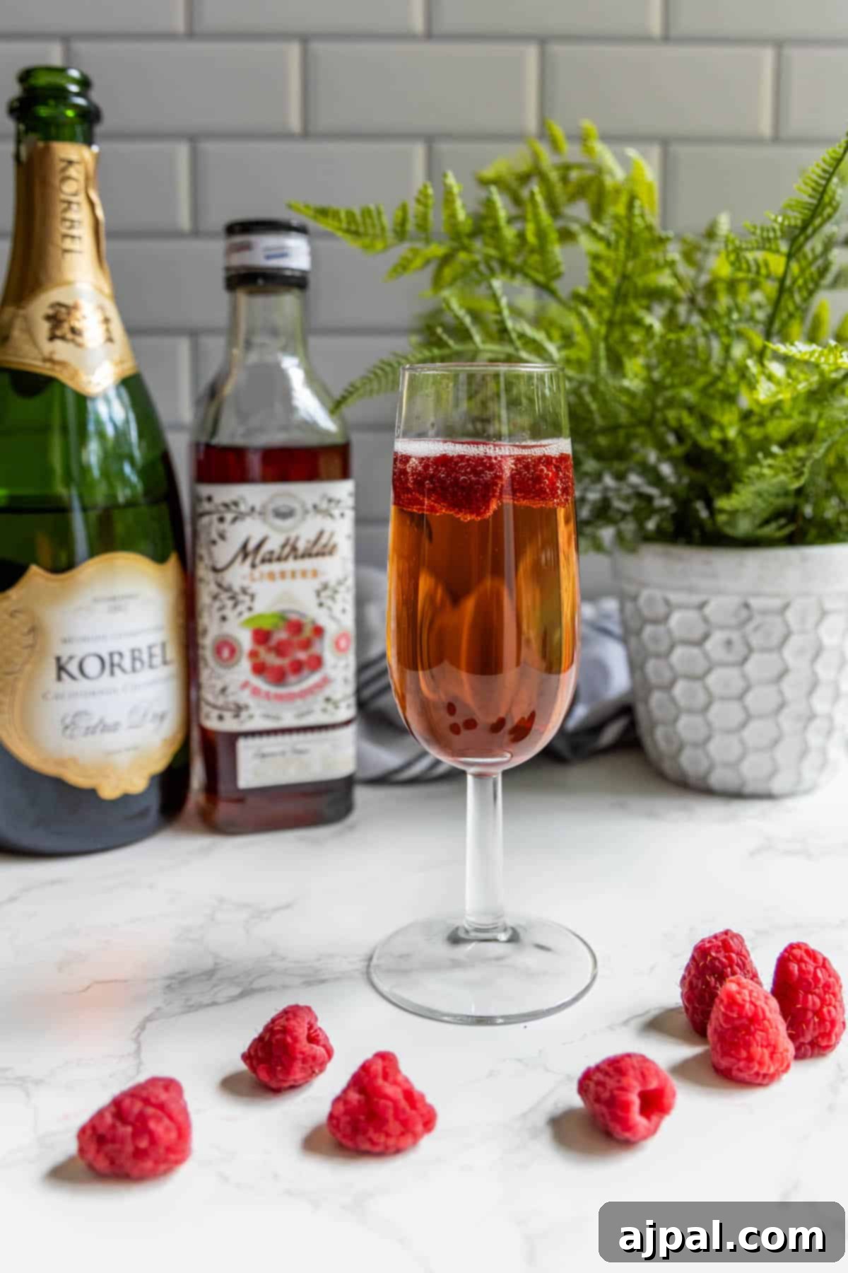 Raspberry Champagne Glow 4 A sparkling raspberry champagne cocktail, garnished with fresh raspberries, sits elegantly next to a bottle of fine wine, creating an inviting and refined scene.