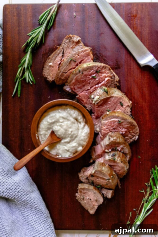 Garlic herb beef tenderloin with sour cream on a cutting board with sprigs of rosemary.