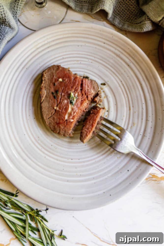 A garlic herb beef tenderloin on a plate with a fork, ready to be served.