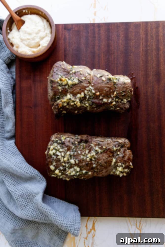 Two lamb chops on a cutting board with a bowl of garlic-herb sauce.