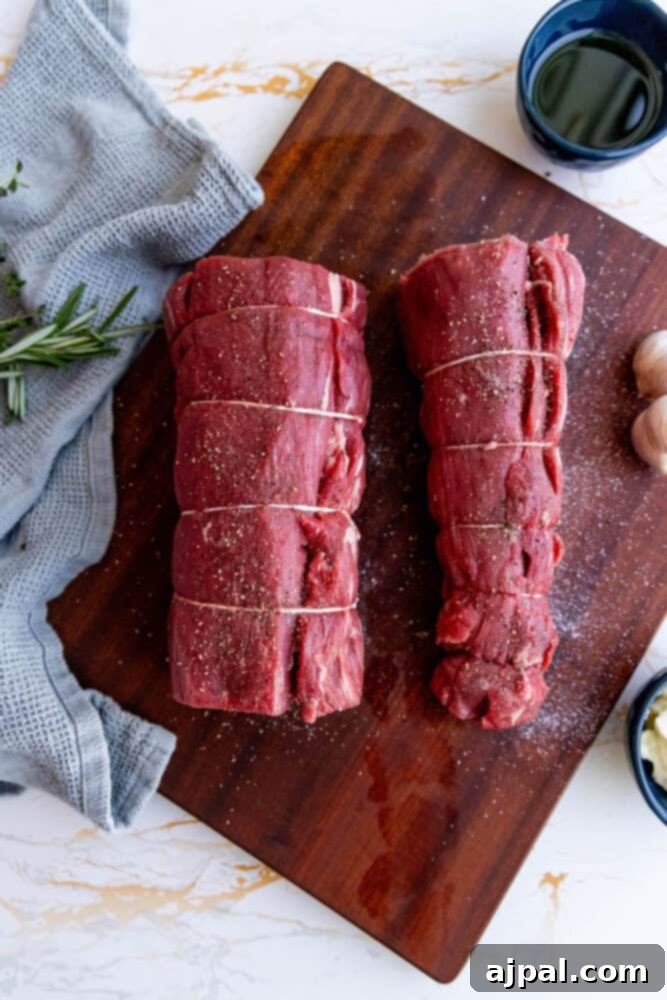 Two pieces of garlic herb beef tenderloin on a wooden cutting board, tied with butcher twine.