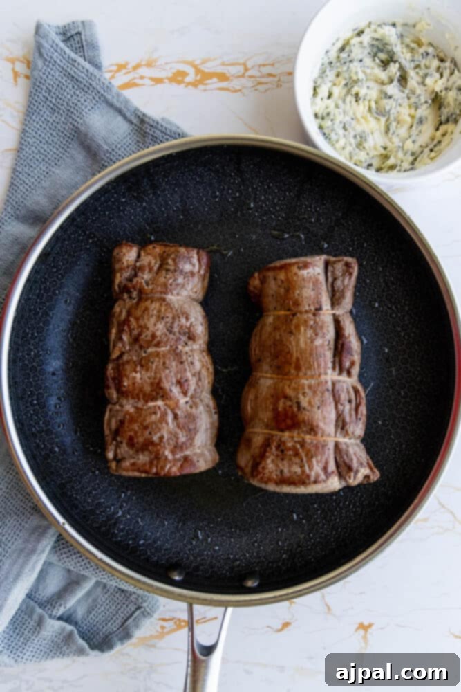 Two garlic herb beef tenderloin steaks in a frying pan with a sauce, searing.