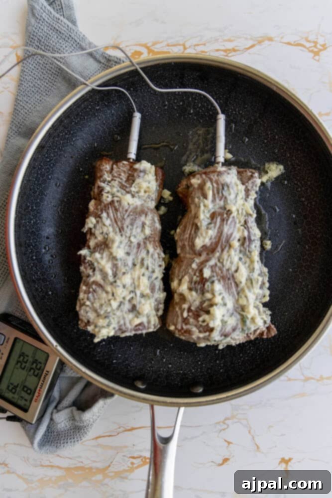 Two garlic herb beef tenderloins sizzling in a frying pan with melted herb butter.