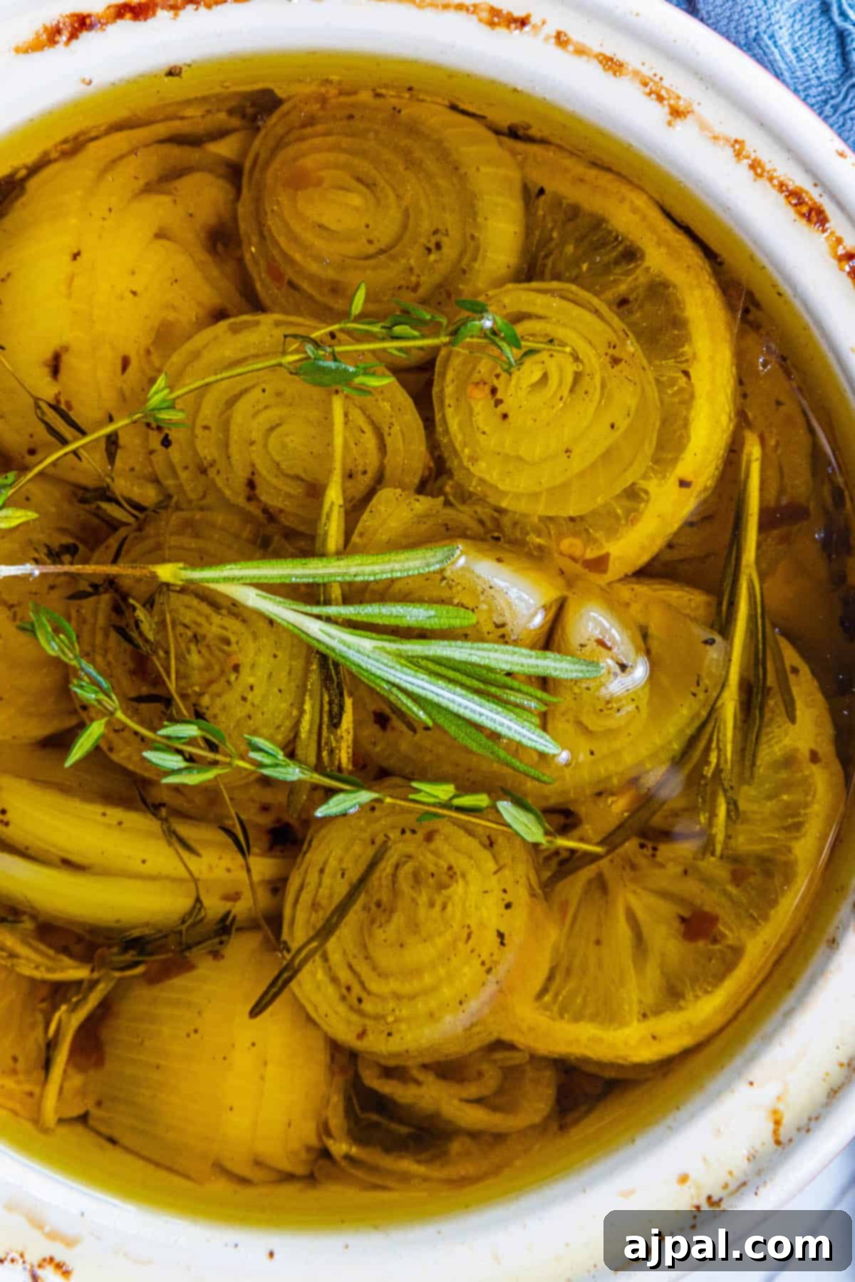 A bowl filled with fresh shallots, onions, and sprigs of fragrant rosemary, ready for confit preparation.