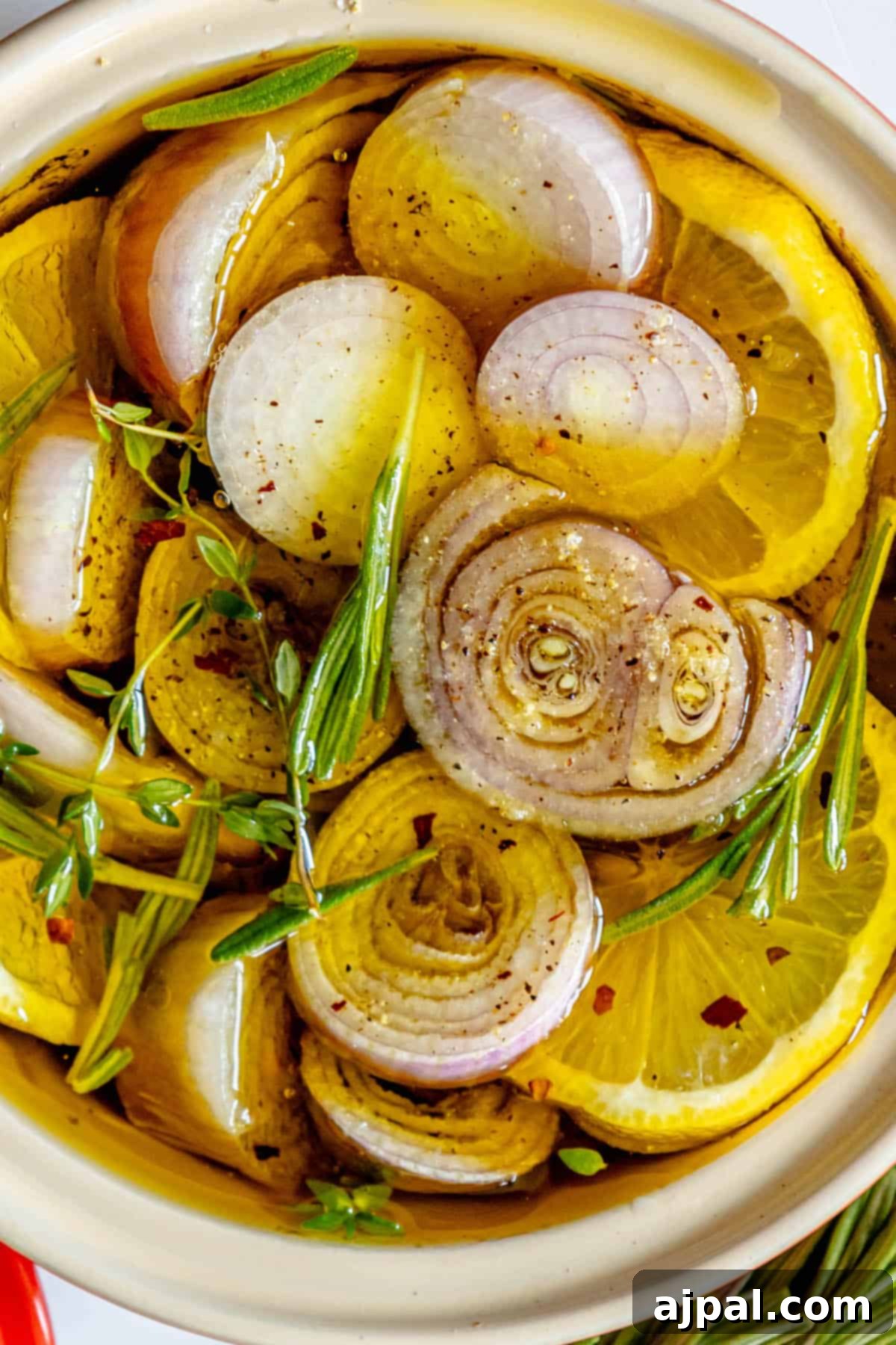 A white bowl filled with beautifully roasted shallots, fresh rosemary, and garlic cloves, highlighting the aromatic ingredients.