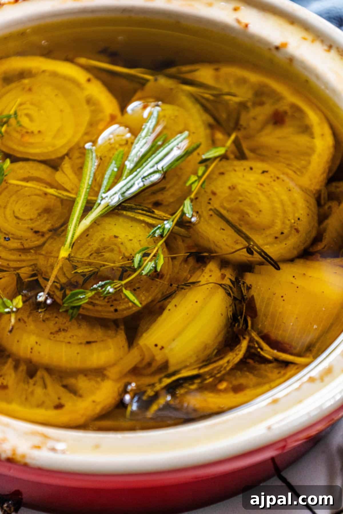A bowl overflowing with glistening confit onions, elegantly topped with a fresh sprig of rosemary for an aromatic touch.