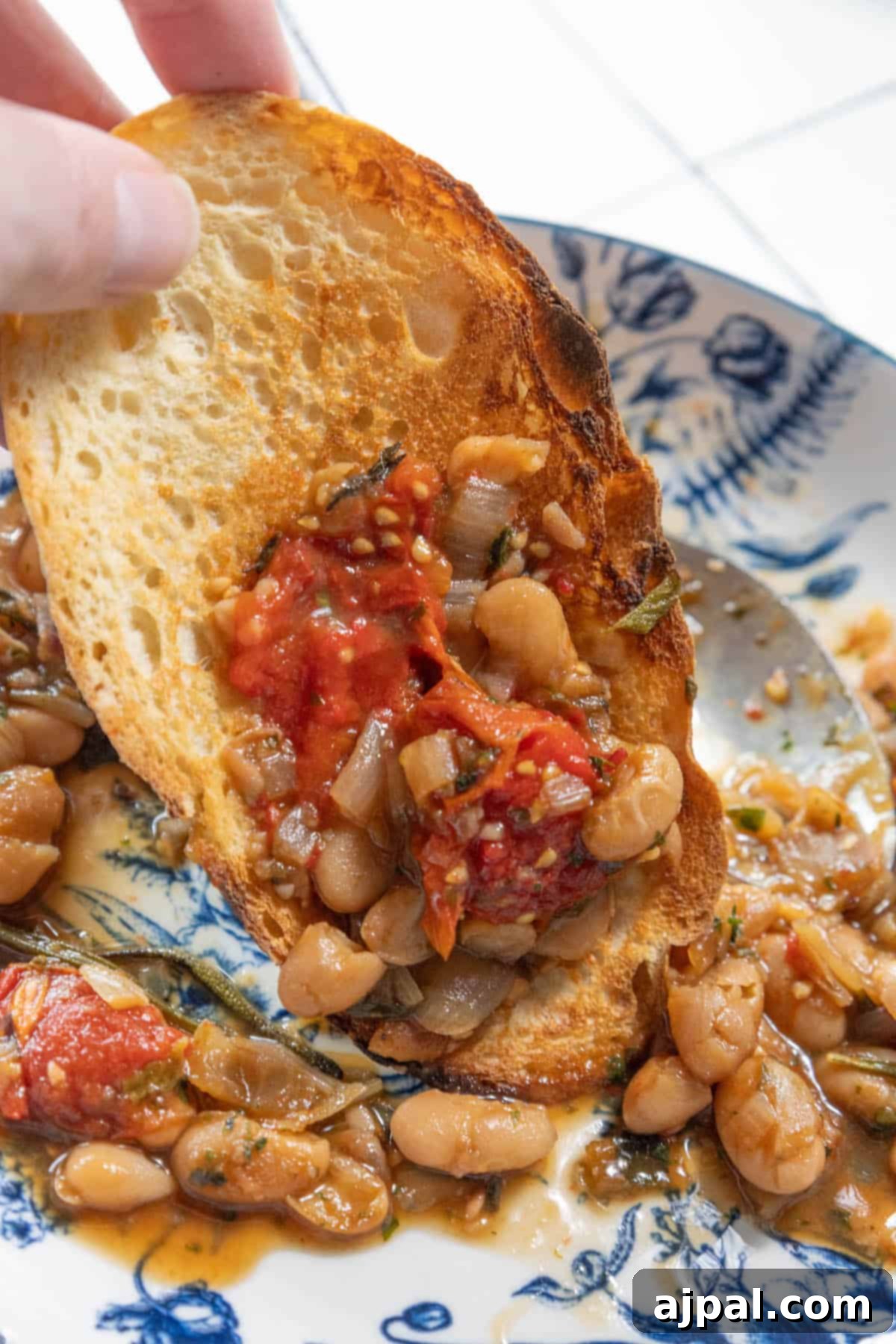 A person holding a piece of toasted bread generously topped with warm, herbed white beans, illustrating a perfect way to enjoy this comforting dish.