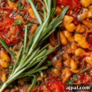 A brothy dish of herbed white beans with a sprig of rosemary, a perfect illustration of this hearty and healthy bean recipe.