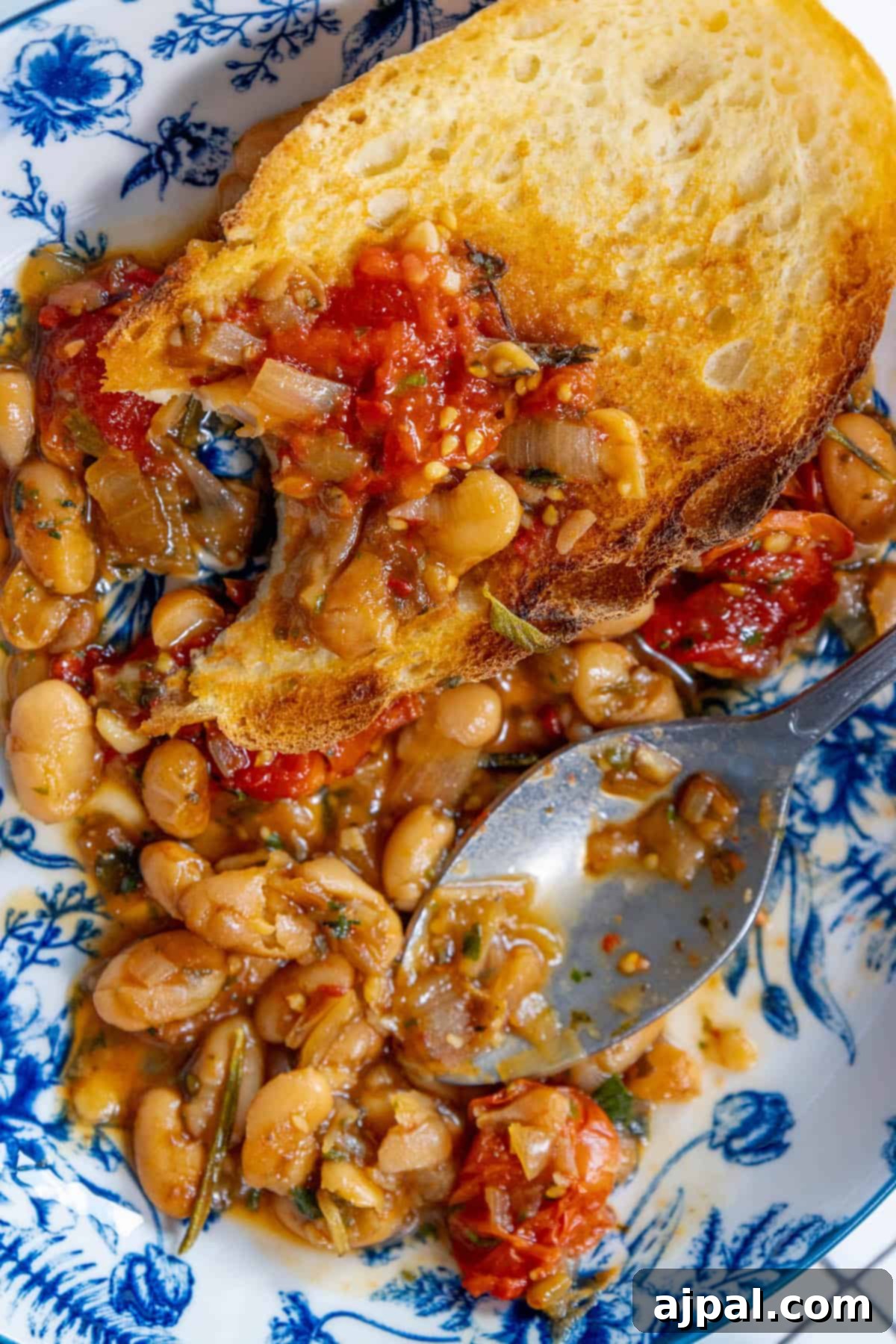 A rustic plate featuring a generous serving of herbed brothy white beans and tomatoes, highlighting the wholesome ingredients and comforting appeal of the dish.