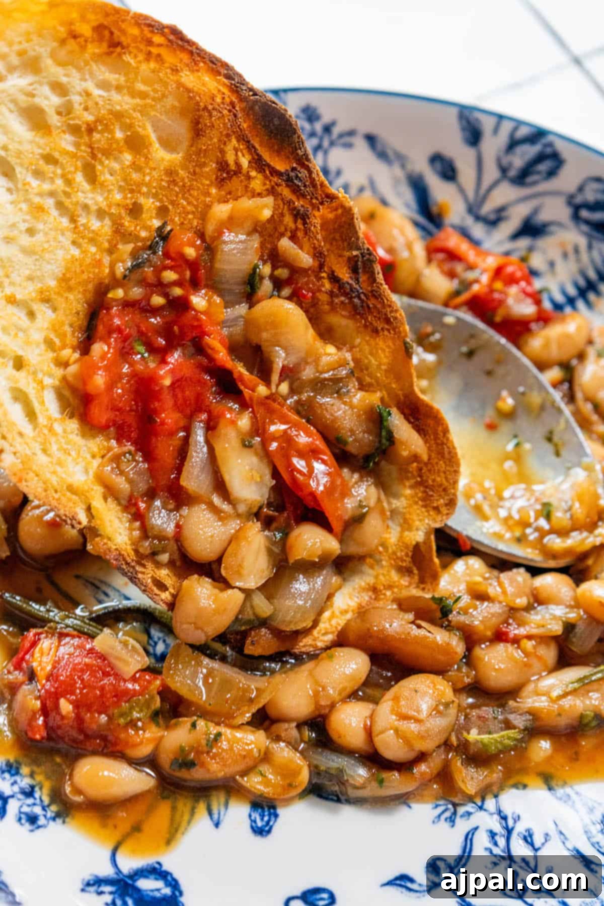 A delightful plate of herbed brothy white beans and tomatoes, served in a deeply flavored, aromatic sauce, showcasing the simplicity and heartiness of this vegan bean recipe.