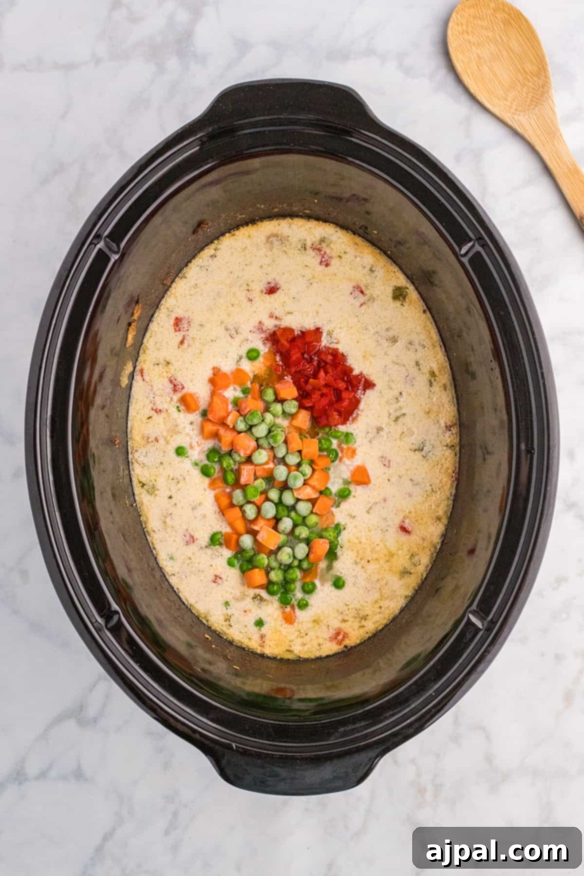 Easy Slow Cooker Chicken a la King 9 A slow cooker full of chicken a la king soup with vegetables and a wooden spoon.