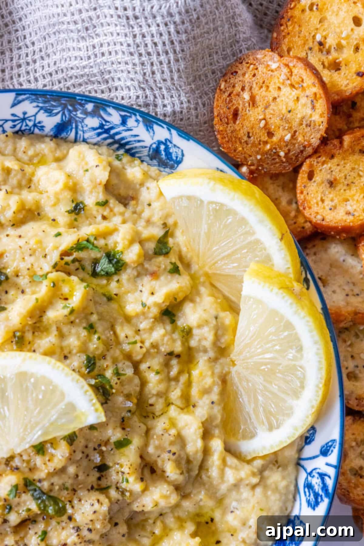 A bowl of roasted hummus with lemon wedges and crackers.