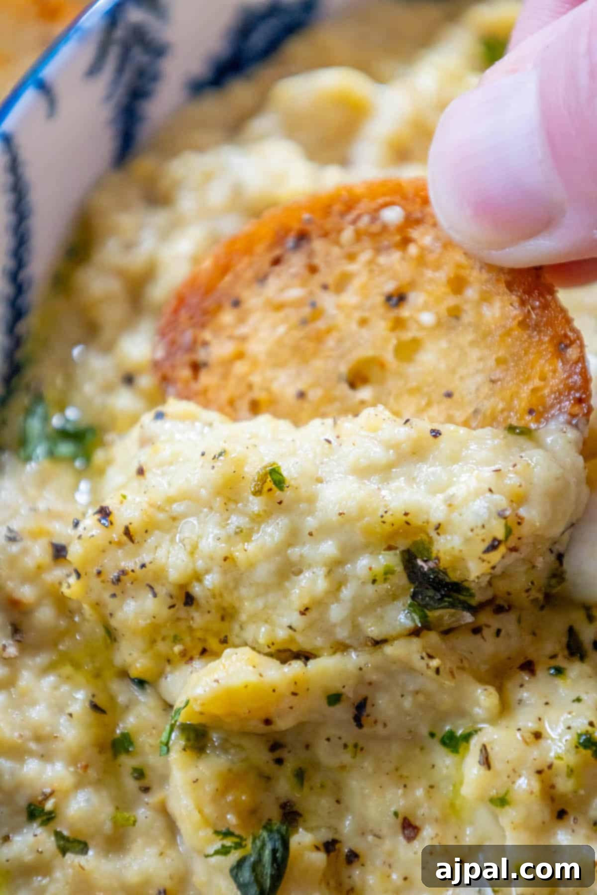 A person dipping artichoke bread into a bowl of roasted dip.