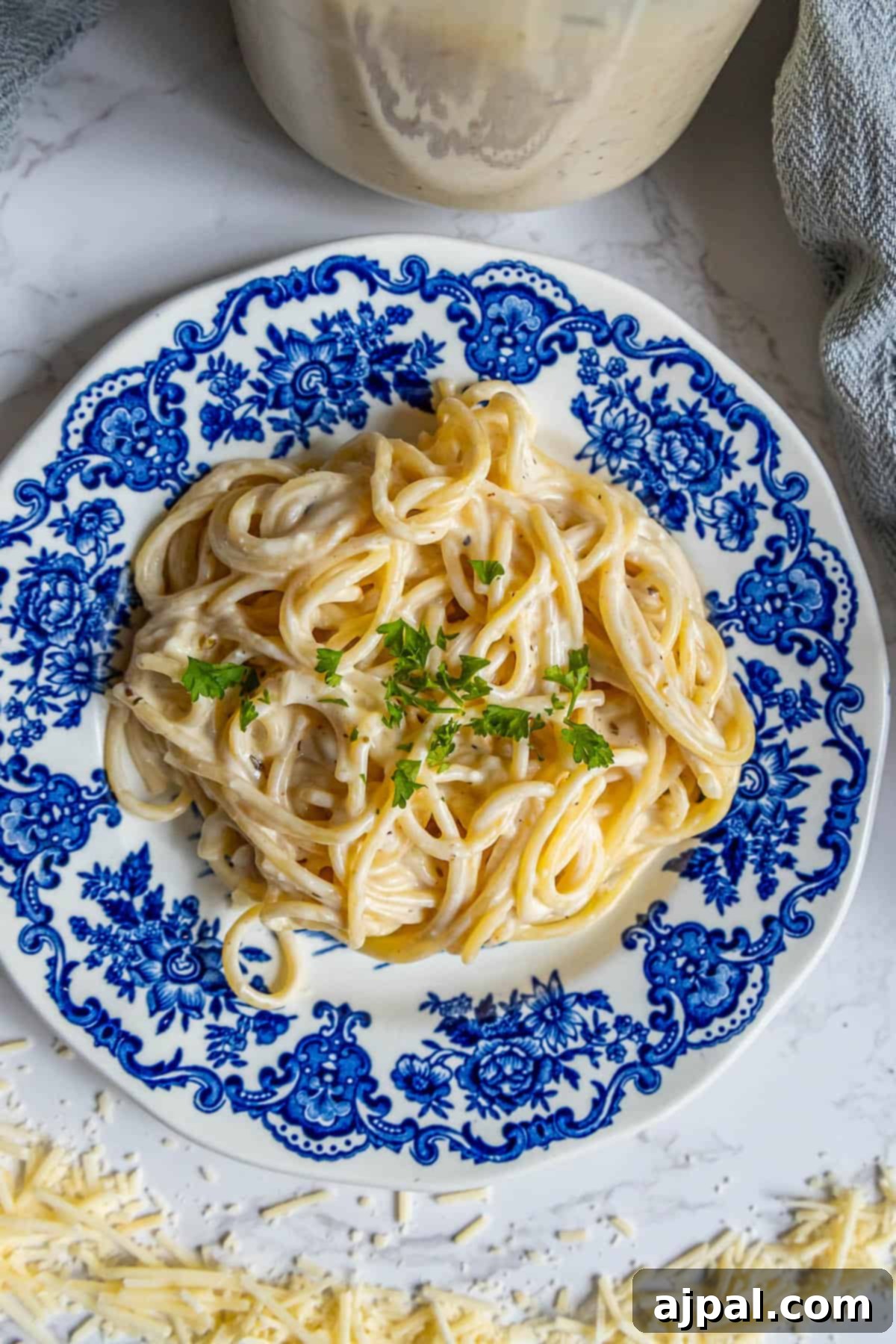 Perfect Homemade Alfredo Sauce 12 A beautifully composed blue and white ceramic plate, artfully arranged with a generous portion of pasta, delicately topped with a sprinkle of freshly grated Parmesan cheese and the rich, creamy Alfredo sauce.