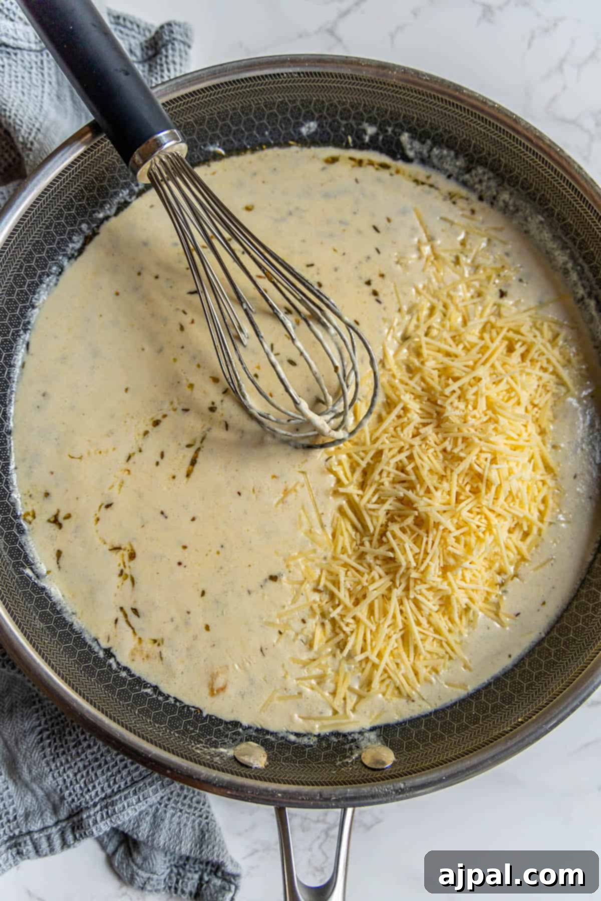 Perfect Homemade Alfredo Sauce 9 A frying pan with a whisk actively stirring the rich, creamy Alfredo sauce as it thickens, showing off its smooth texture.
