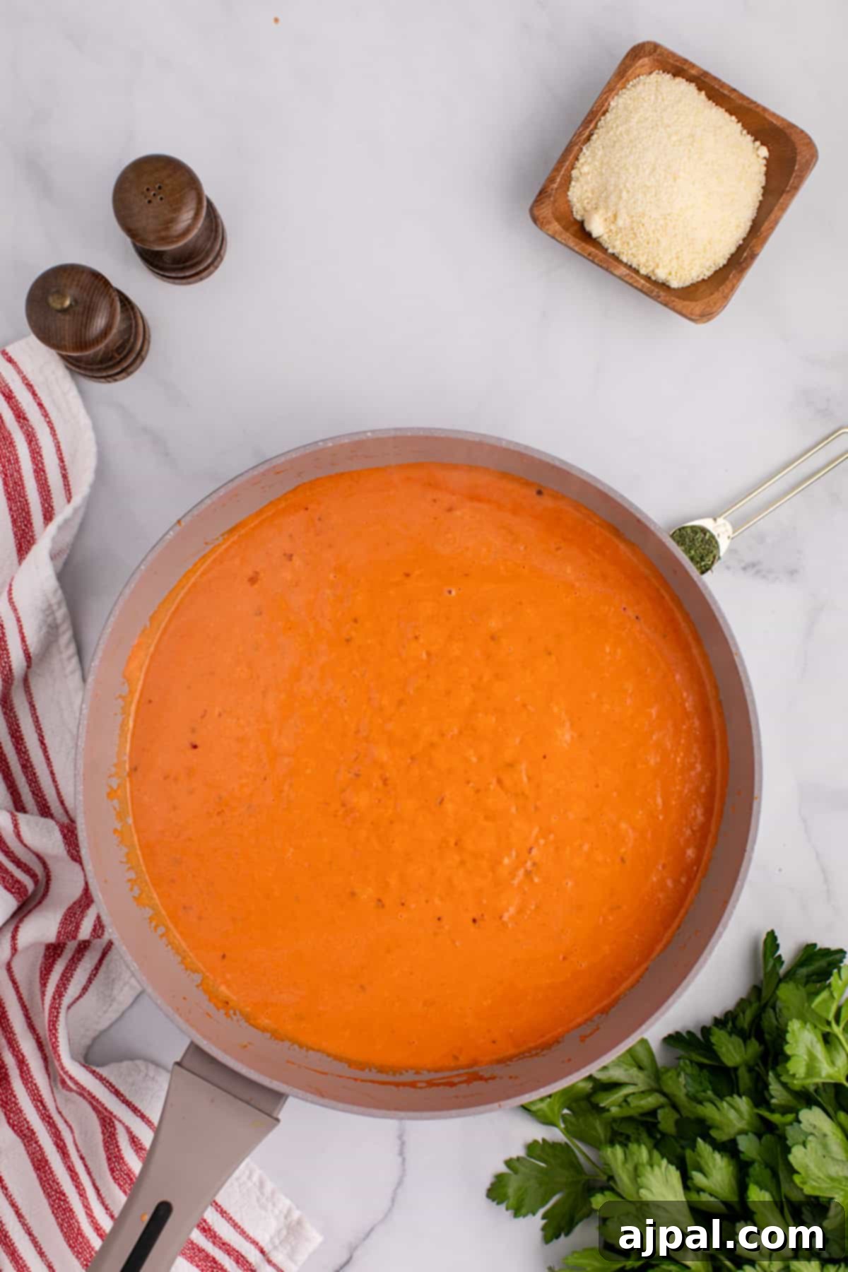Spicy tomato sauce in a pan with parmesan cheese and parsley being prepared to be served with rigatoni pasta.