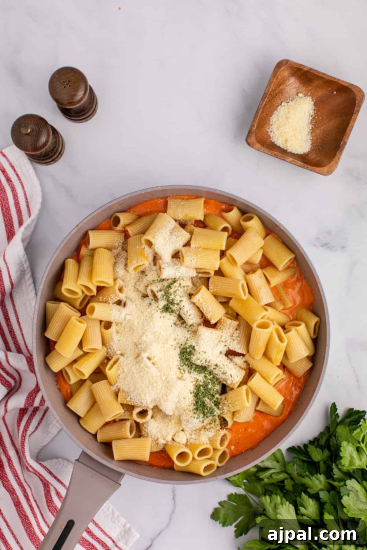 Rigatoni pasta cooked in a pan, coated in sauce with parmesan cheese and parsley.