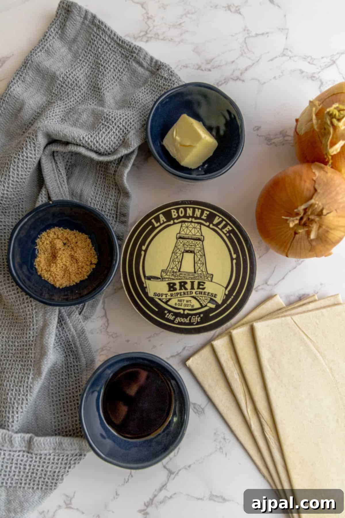 A vibrant array of fresh ingredients for brie tarts laid out on a table, including puff pastry, onions, and brie cheese.
