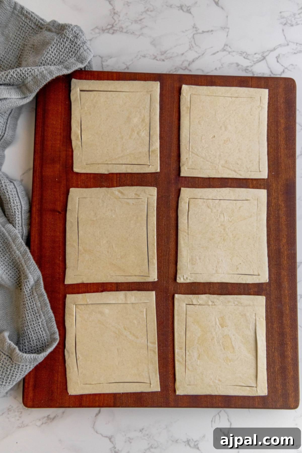 Puff pastry sheets expertly cut into squares, showing the L-shape incisions for shaping into tarts.
