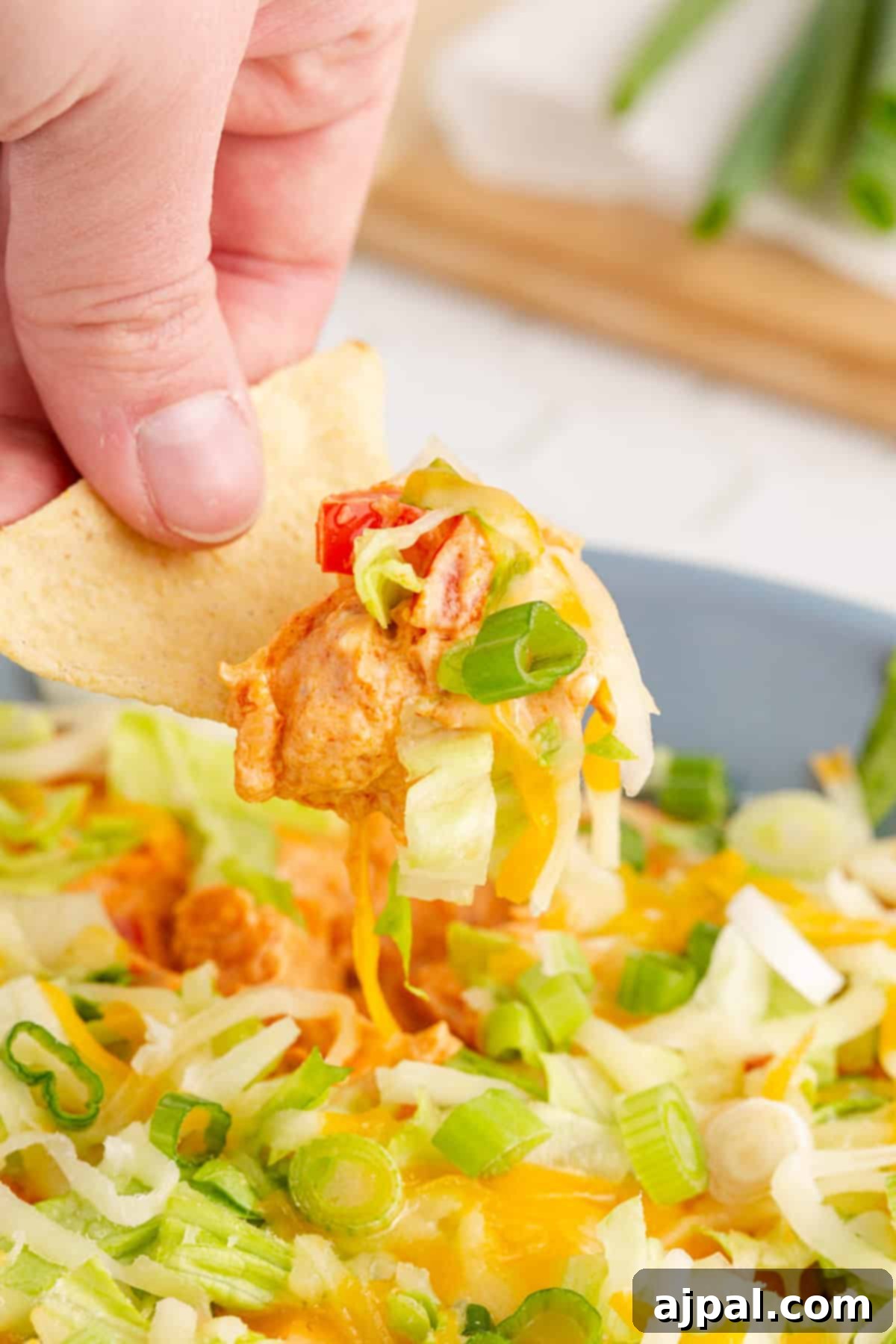 Zesty Taco Dip 2 A person dipping a tortilla chip into a hot, cheesy taco dip, surrounded by fresh toppings.