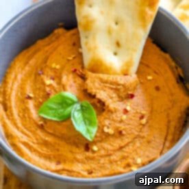 A bowl of hummus with pita chips on a wooden cutting board.